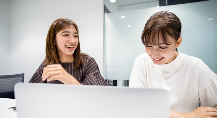 Two women sit side by side in a bright meeting room