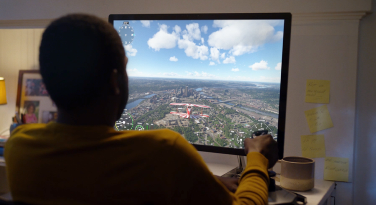 A person sitting at a desk plays a flight simulation game on a large monitor