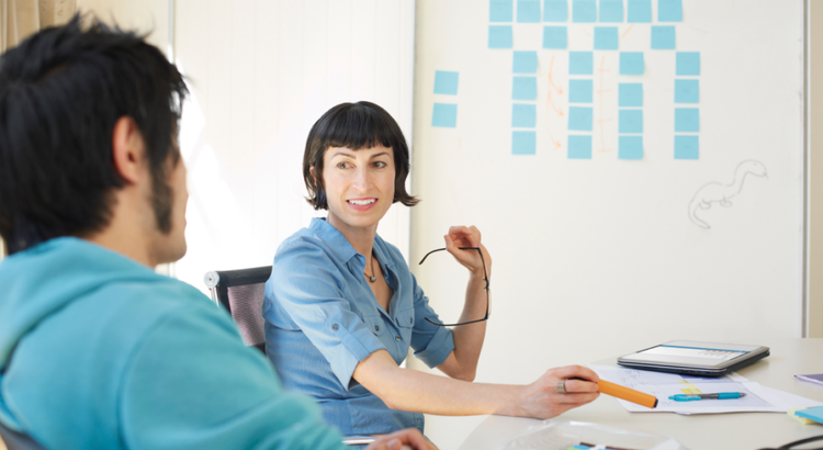 Two people sit at a table in a bright office space