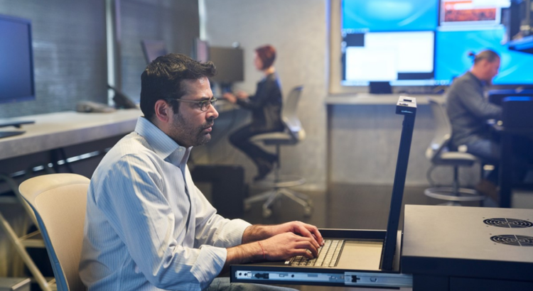 Person in a button-down shirt types on a pull-out keyboard in a control room