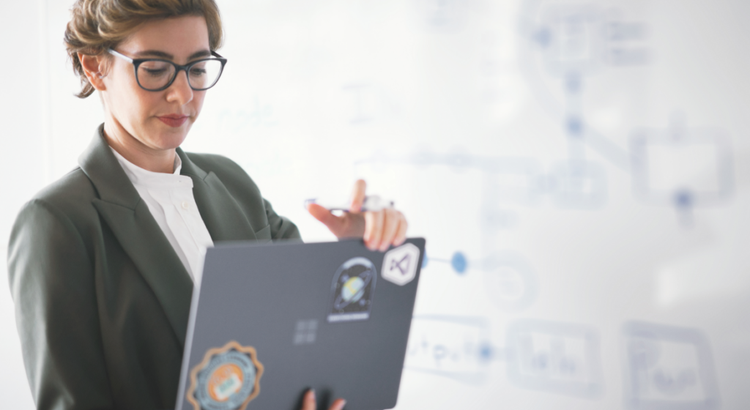 Person wearing glasses and a blazer stands in front of a whiteboard covered