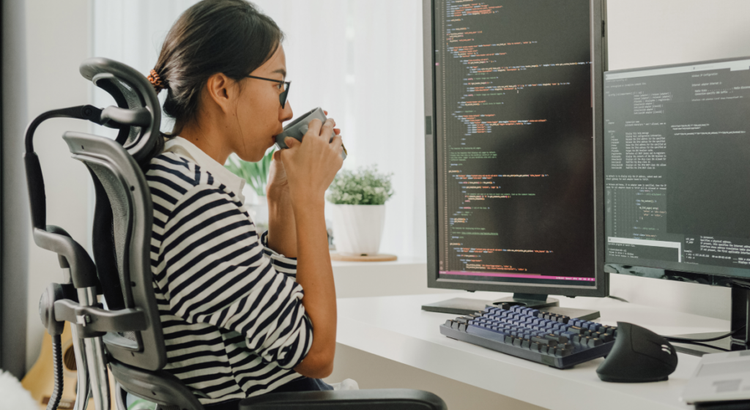 Person in a striped shirt sits at a desk with dual monitors displaying code