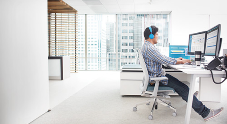 A man wearing blue headphones works at a modern white desk