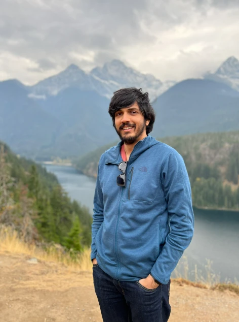 A man standing on a hill with a lake and mountains in the background