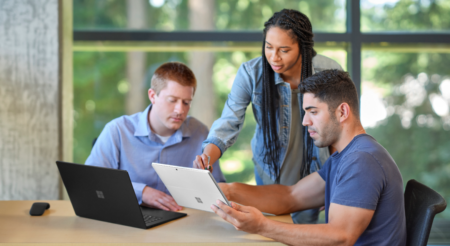 Three people collaborating in an office on laptops.